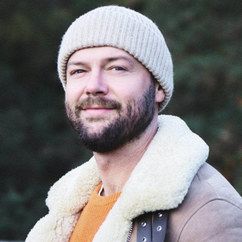 Portrait of Olivier Passebecq, smiling, in a knitted hat and orange jumper